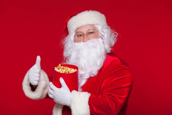 Babbo Natale tradizionale guardare la TV, mangiare popcorn. Natale. Sfondo rosso. emozioni paura sorpresa — Foto Stock