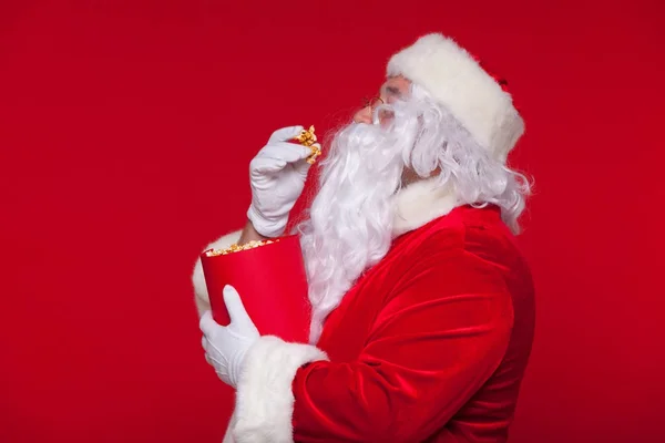 Traditionelle Weihnachtsmann vor dem Fernseher, essen Popcorn. Weihnachten. roter Hintergrund. Emotionen fürchten Überraschung — Stockfoto