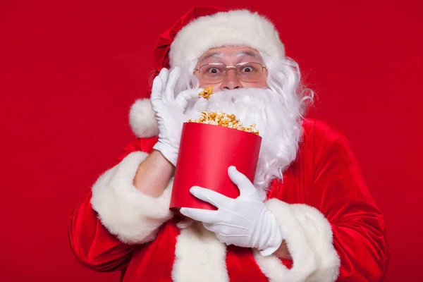 Père Noël traditionnel regardant la télé, mangeant du pop-corn. Noël. Fond rouge. émotions peur surprise — Photo