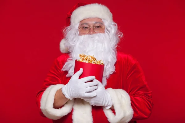 Traditionelle Weihnachtsmann vor dem Fernseher, essen Popcorn. Weihnachten. roter Hintergrund. Emotionen fürchten Überraschung — Stockfoto