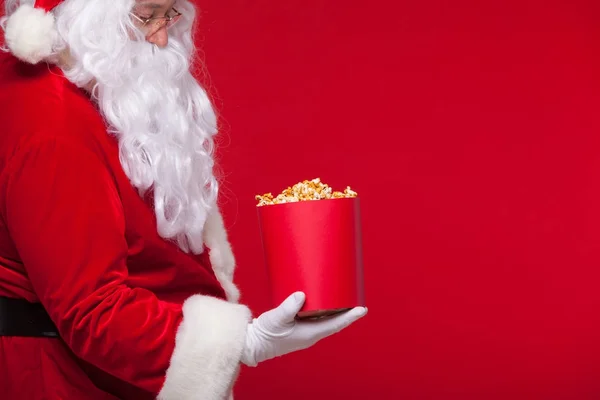 Natale. Foto di Babbo Natale mano guantata Con un secchio rosso con popcorn, su uno sfondo rosso — Foto Stock