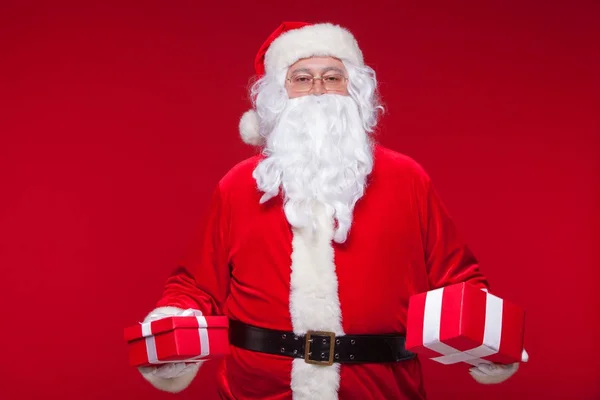 Navidad. Foto Santa Claus dando regalo de Navidad y mirando a la cámara, sobre un fondo rojo — Foto de Stock