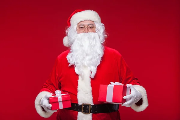 Weihnachten. photo santa claus macht Weihnachtsgeschenk und blickt in die Kamera, auf rotem Hintergrund — Stockfoto