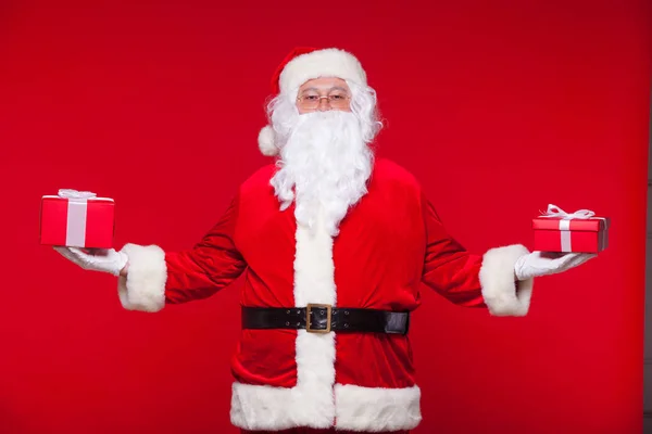 Navidad. Foto Santa Claus dando regalo de Navidad y mirando a la cámara, sobre un fondo rojo — Foto de Stock