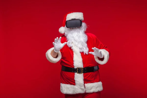 Santa Claus vistiendo gafas de realidad virtual, sobre fondo rojo. Navidad —  Fotos de Stock