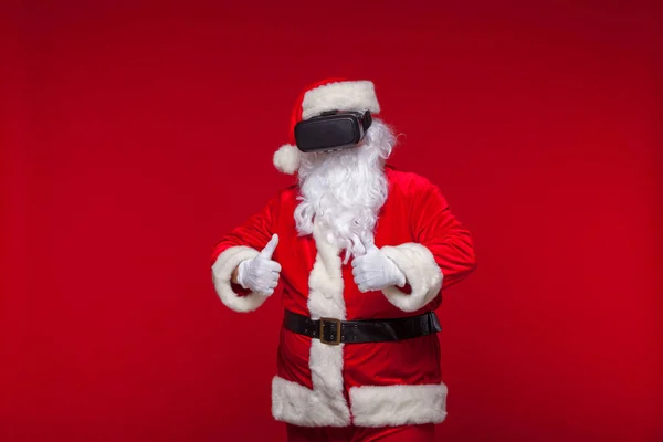 Santa Claus vistiendo gafas de realidad virtual, sobre fondo rojo. Navidad — Foto de Stock