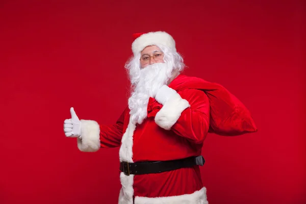 Navidad. santa claus con gran bolso en el hombro es sobre fondo rojo —  Fotos de Stock