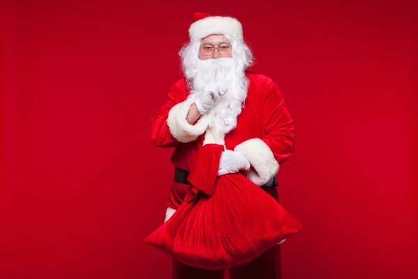 Navidad. santa claus con gran bolso en el hombro es sobre fondo rojo — Foto de Stock