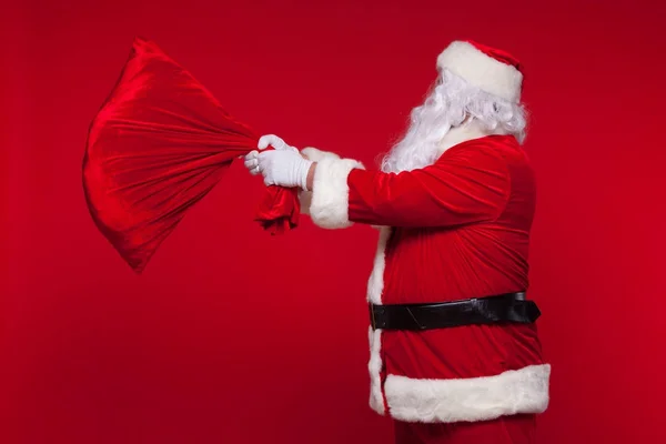 Navidad. santa claus con gran bolso en el hombro es sobre fondo rojo —  Fotos de Stock