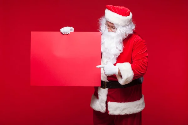 Weihnachtsmann zeigt auf leeres Werbebanner auf rotem Hintergrund mit rotem Blatt — Stockfoto
