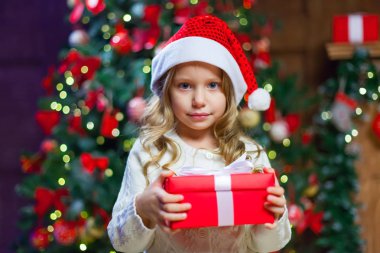 Küçük kız bir Noel hediyesi tutan ağaç başına oturmuş 
