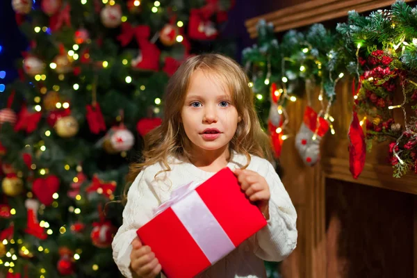 Niña sentada junto al árbol sosteniendo un regalo de Navidad — Foto de Stock