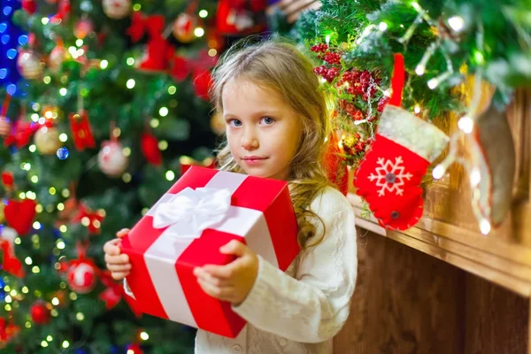 Niña sentada junto al árbol sosteniendo un regalo de Navidad — Foto de Stock