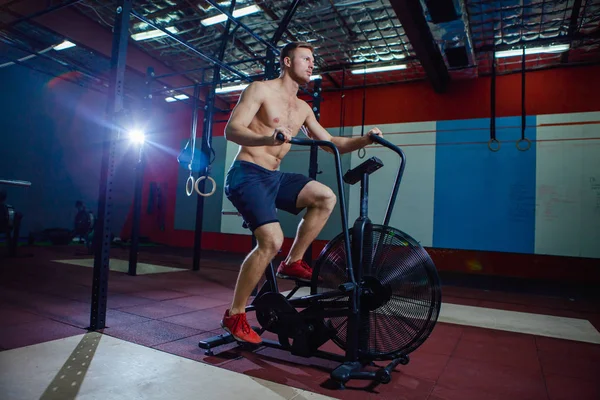 Passar ung man använder motionscykel på gymmet. Fitness man använder luft cykel för konditionsträning på cross träning gym. — Stockfoto