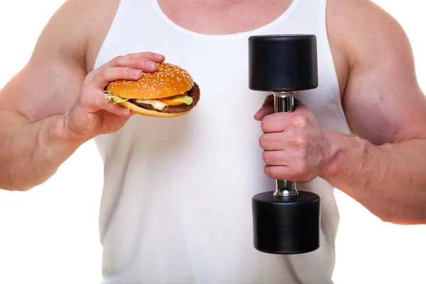 Hombre gordo con una hamburguesa sostiene pesas aisladas en blanco. El concepto de elegir entre alimentos nocivos y un estilo de vida saludable. Retrato de una persona con sobrepeso que estropeó la comida saludable. Comida chatarra — Foto de Stock