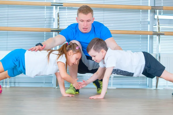 Группа детей, занимающихся детской гимнастикой в тренажерном зале с учителем. Счастливые спортивные дети в спортзале. бар упражнения. доска . — стоковое фото