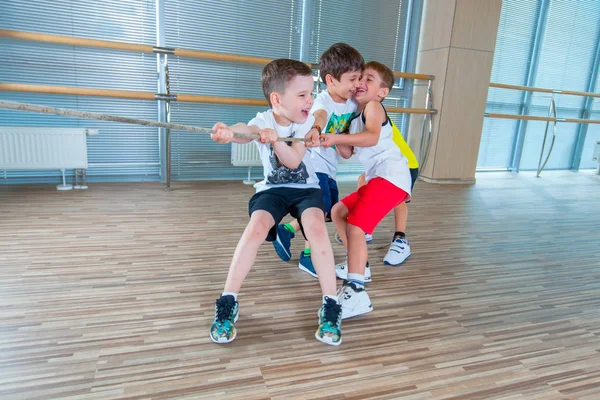 Barn och fritid, grupp av glad multietnisk skola barn leka dragkamp med rep i gymmet — Stockfoto