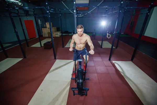 Ajuste joven usando bicicleta estática en el gimnasio. Fitness masculino usando bicicleta neumática para entrenamiento cardiovascular en el gimnasio de entrenamiento cruzado . —  Fotos de Stock