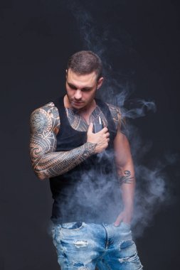 Vaper. Dövmeli kas bir gövde adamla koyu arka plan üzerinde elektronik sigara duman