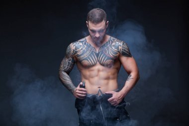 Vaper. Dövmeli bir kaslı çıplak gövde adamla koyu arka plan üzerinde elektronik sigara duman
