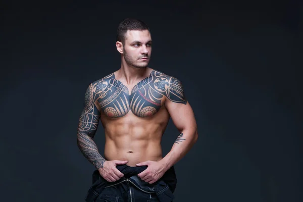 El hombre con un torso desnudo muscular con tatuajes en el fondo oscuro. ABS —  Fotos de Stock