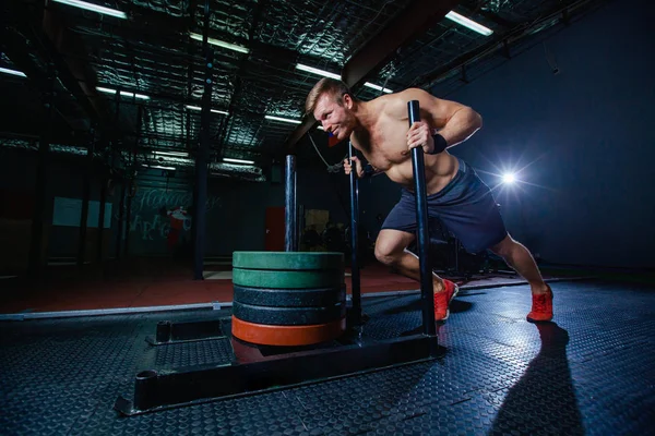 Slitta spingere uomo spingendo pesi esercizio di allenamento in palestra. Stile Cross fit — Foto Stock