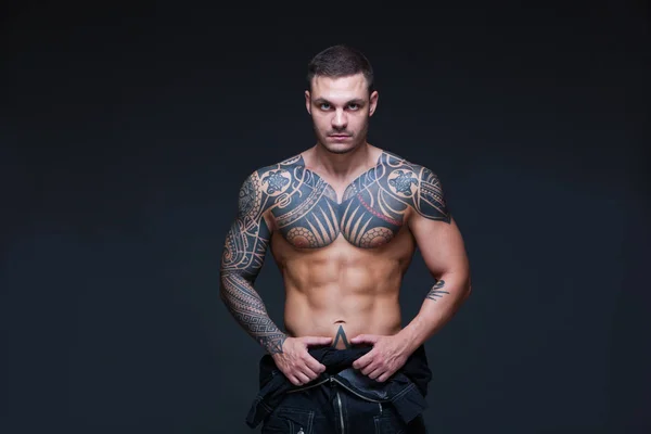 El hombre con un torso desnudo muscular con tatuajes en el fondo oscuro. ABS —  Fotos de Stock