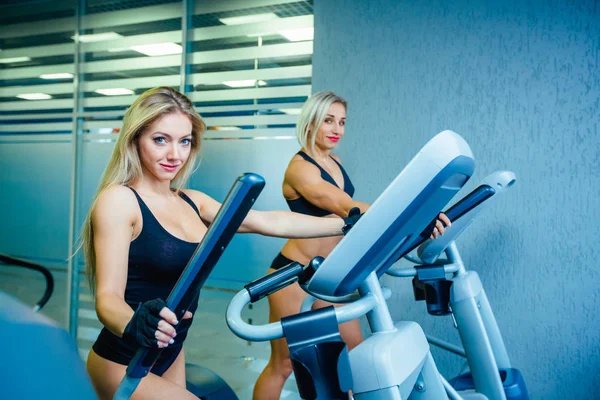 Positif deux amies s'entraînant sur des entraîneurs elliptiques dans un club de fitness, concept de style de vie. entraînement cardio, combustion des graisses, perte de poids — Photo