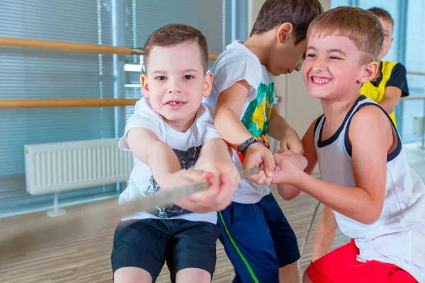 Kinder und Freizeit, Gruppe fröhlicher multiethnischer Schulkinder, die Tauziehen mit Seil in der Turnhalle spielen — Stockfoto