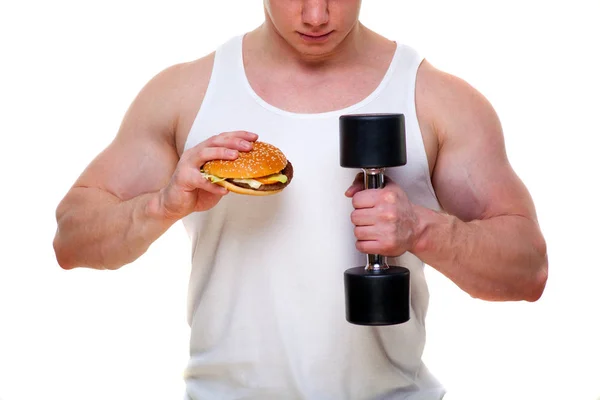 Hombre gordo con una hamburguesa sostiene pesas aisladas en blanco. El concepto de elegir entre alimentos nocivos y un estilo de vida saludable. Retrato de una persona con sobrepeso que estropeó la comida saludable. Comida chatarra —  Fotos de Stock