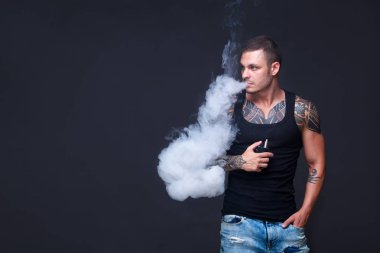 Vaper. Dövmeli kas bir gövde adamla koyu arka plan üzerinde elektronik sigara duman