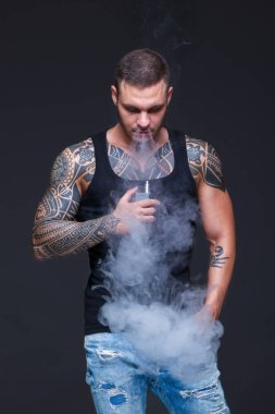 Vaper. Dövmeli kas bir gövde adamla koyu arka plan üzerinde elektronik sigara duman
