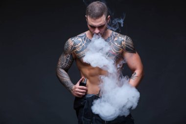 Vaper. Dövmeli bir kaslı çıplak gövde adamla koyu arka plan üzerinde elektronik sigara duman