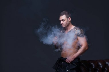 Vaper. Dövmeli bir kaslı çıplak gövde adamla koyu arka plan üzerinde elektronik sigara duman