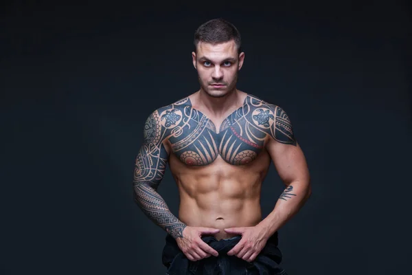 El hombre con un torso desnudo muscular con tatuajes en el fondo oscuro. ABS —  Fotos de Stock