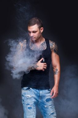Vaper. Dövmeli kas bir gövde adamla koyu arka plan üzerinde elektronik sigara duman