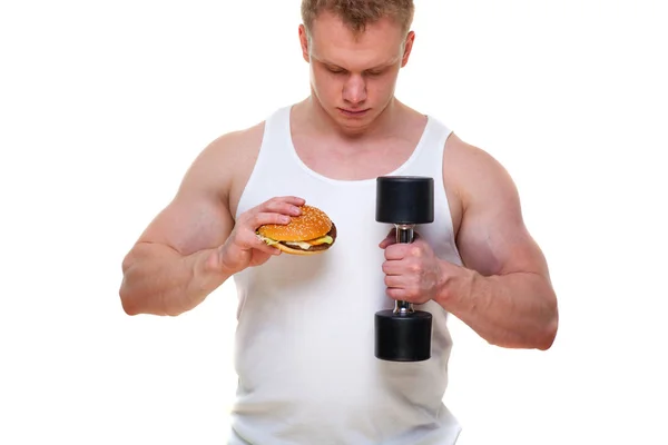 Şişko bir hamburger ile üzerine beyaz izole dumbbells tutar. Zararlı gıda ve sağlıklı bir yaşam tarzı arasında seçim yapma kavramı. Sağlıklı yemek şımarık kilolu kişi portresi. Önemsiz yemek — Stok fotoğraf