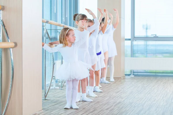 Jovens bailarinas ensaiando na aula de balé. Eles realizam diferentes exercícios coreográficos. Eles estão em diferentes posições perto do ballet barr . — Fotografia de Stock