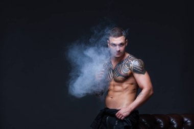 Vaper. Dövmeli bir kaslı çıplak gövde adamla koyu arka plan üzerinde elektronik sigara duman