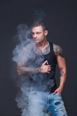 Vaper. Dövmeli kas bir gövde adamla koyu arka plan üzerinde elektronik sigara duman