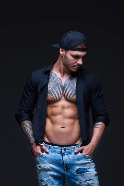 Людина одягнені сині джинси, чорні сорочки і чорний Бейсболки з татуювання на темному тлі. ABS — стокове фото