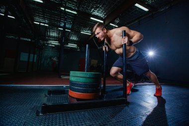 kızak itme adam spor salonunda ağırlık egzersiz egzersiz bastırıyor. Çapraz uygun stil