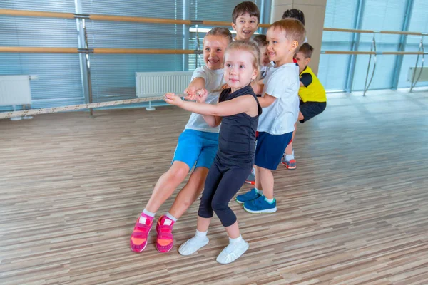 Barn och fritid, grupp av glad multietnisk skola barn leka dragkamp med rep i gymmet — Stockfoto