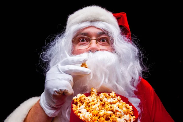 No Natal. Foto de Papai Noel mão luva Com um balde vermelho com pipoca, em um fundo preto — Fotografia de Stock