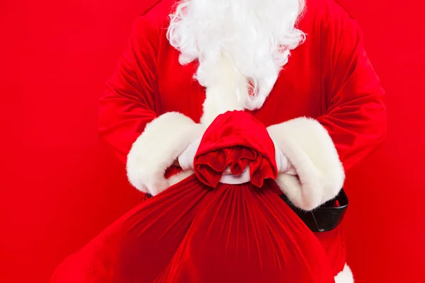 Papai Noel mão segurando saco vermelho cheio de presentes mais — Fotografia de Stock