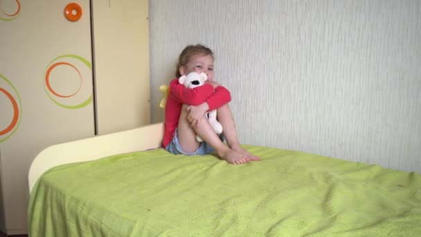 Huiselijk geweld. De vader bedreigt het kind met een riem. Triest meisje met een blauw oog zittend op het bed, die een speelgoedbeer vasthoudt en zijn ogen sluit met zijn handen. Angst. — Stockvideo