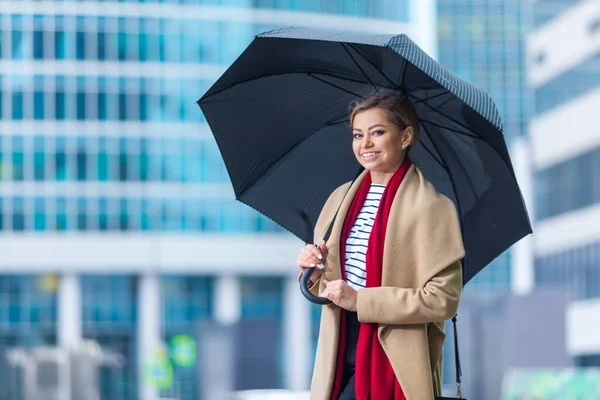 Regen. Outdoor Lifestyle Mode Porträt von atemberaubenden brünetten Mädchen. zu Fuß auf der Stadtstraße. Einkaufen gehen. Er trug einen schicken weißen Mantel, ein rotes Halstuch und einen schwarzen Regenschirm. Geschäftsfrau. — Stockfoto