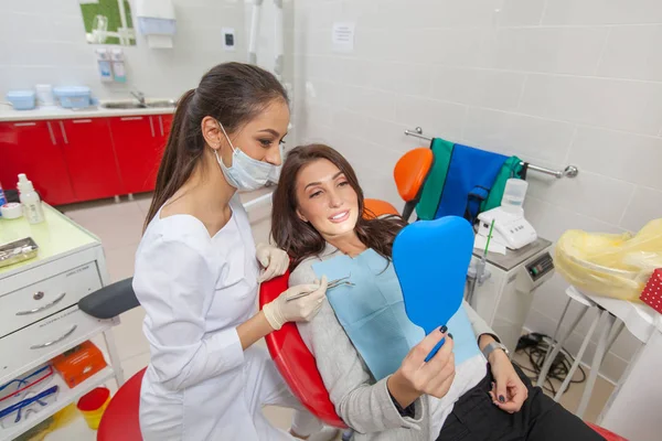 Zahnarzt. eine Frau in der Zahnarztpraxis untersucht ihre Zähne im Spiegel und lächelt. — Stockfoto