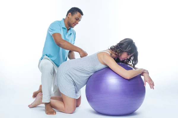 A young black man helps his white wife with birth pain with a ball. Partnered birth, partnered delivery. Isolated white background. — Stock Photo, Image