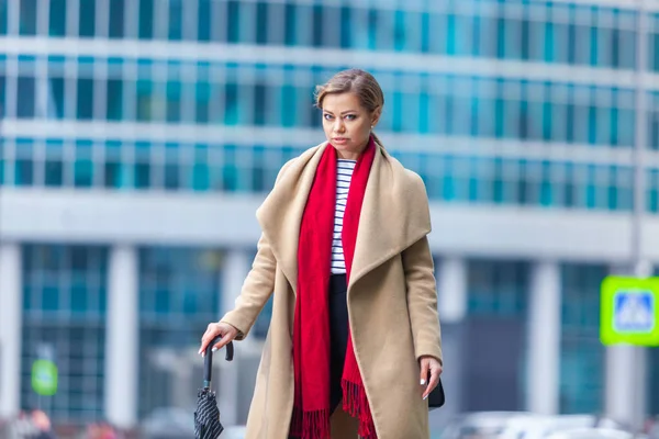 Buiten lifestyle modeportret van een prachtig brunette meisje. Wandelen op straat. Winkelen. Draag stijlvolle witte jas, rode neksjaal, zwarte paraplustok. Zakelijke vrouw. — Stockfoto